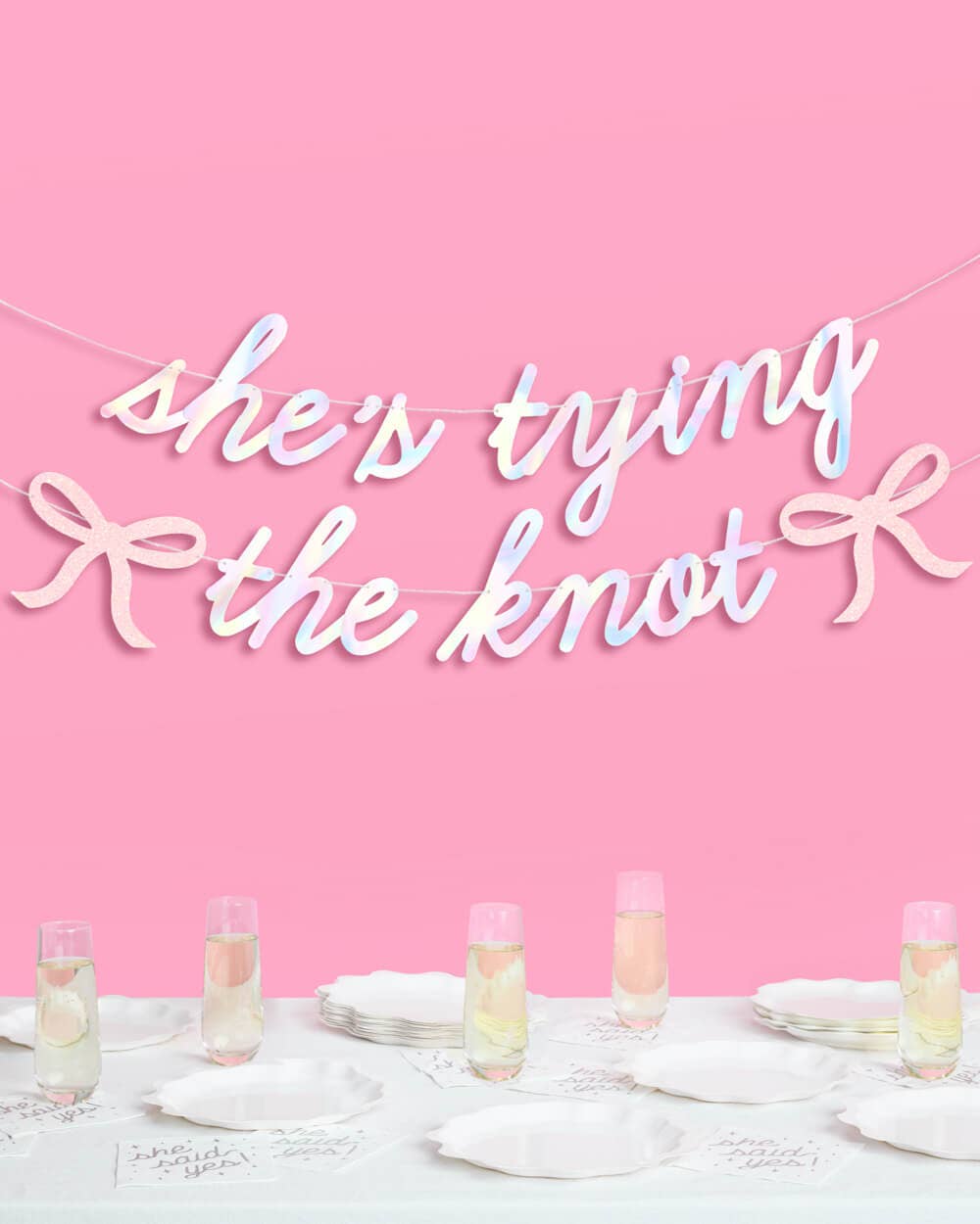 She's Tying the Knot iridescent banner hung above bridal shower table with champagne flutes and white plates