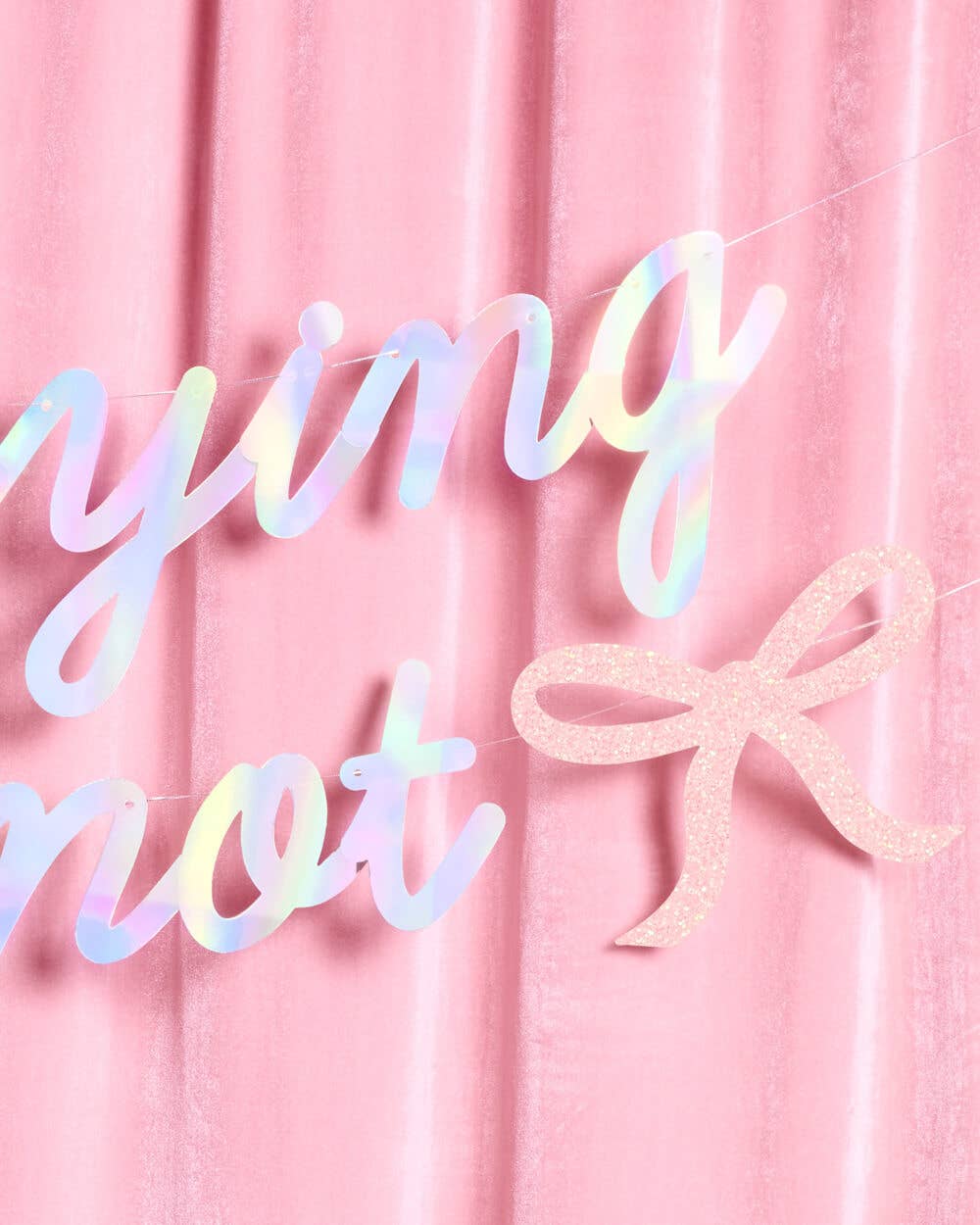 Close-up of iridescent foil script and pink glitter bow detail on She's Tying the Knot banner against pink velvet