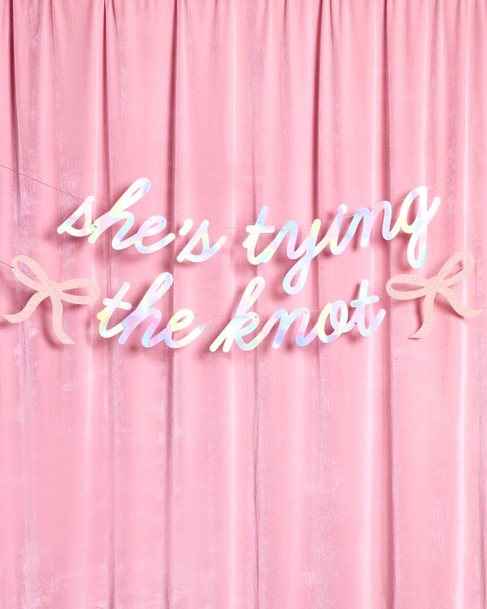 She's Tying the Knot iridescent banner hung on pink velvet backdrop for bridal shower