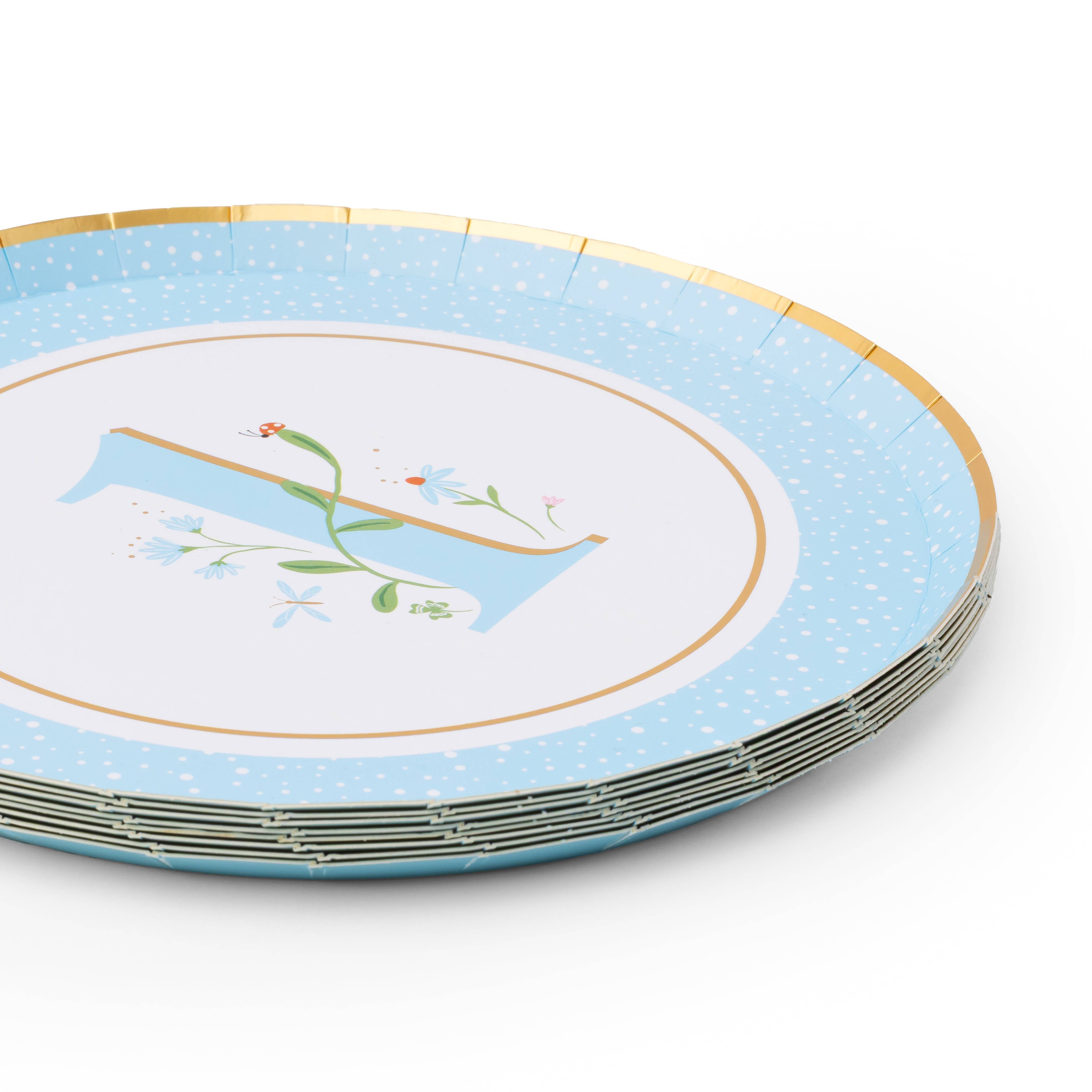 Angled stack of sky blue first birthday paper plates with floral illustrated number 1 and gold foil rim on white background
