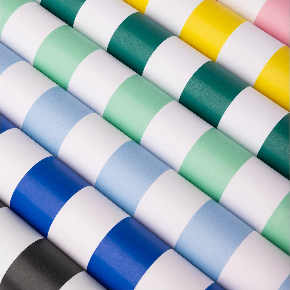 Diagonal close‑up of rolled paper runners in multiple colors, highlighting the sky‑blue and white stripe roll in front.
