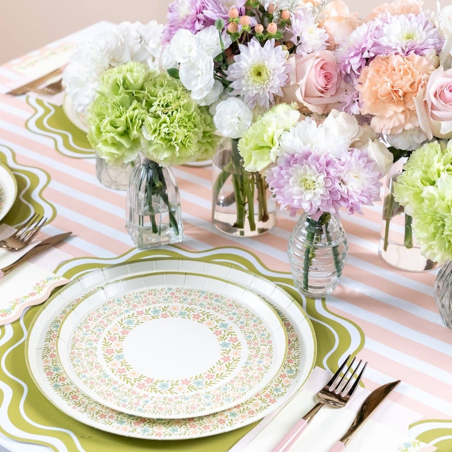 Close-up of pink striped table runner with floral plates and glass vases