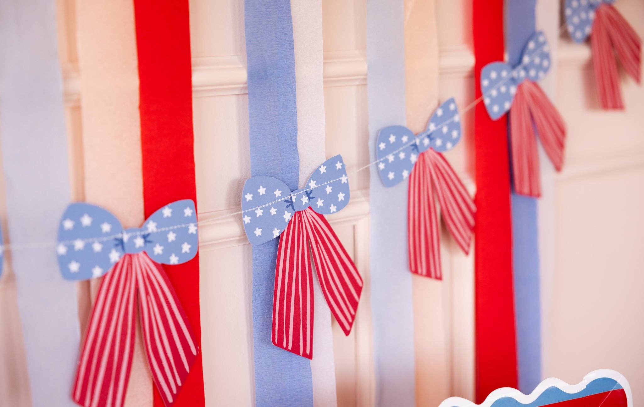 Close-up detail of stars and stripes paper bows on cream twine with blue star-print tops and red-striped tails against red and blue streamers