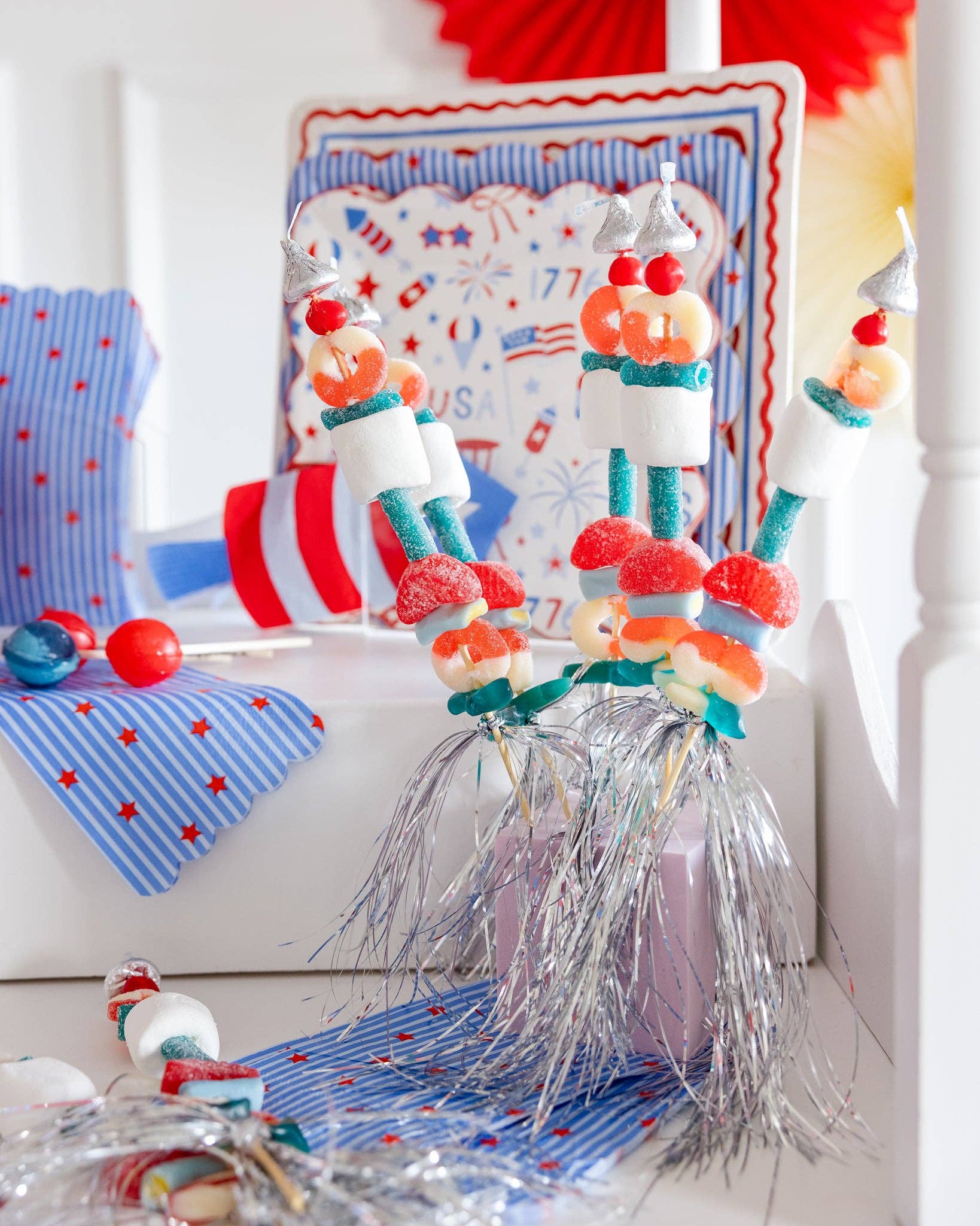 Stars and stripes paper guest napkins displayed on a patriotic party tablescape with red, white, and blue candy kabobs and coordinating party plates