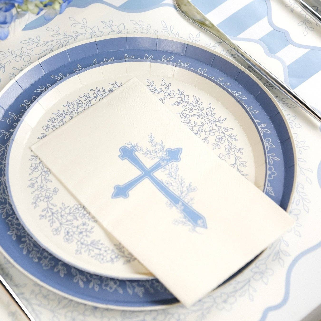 A close up view of a blue and white paper plate with a blue botanical cross guest towel for a religious event.