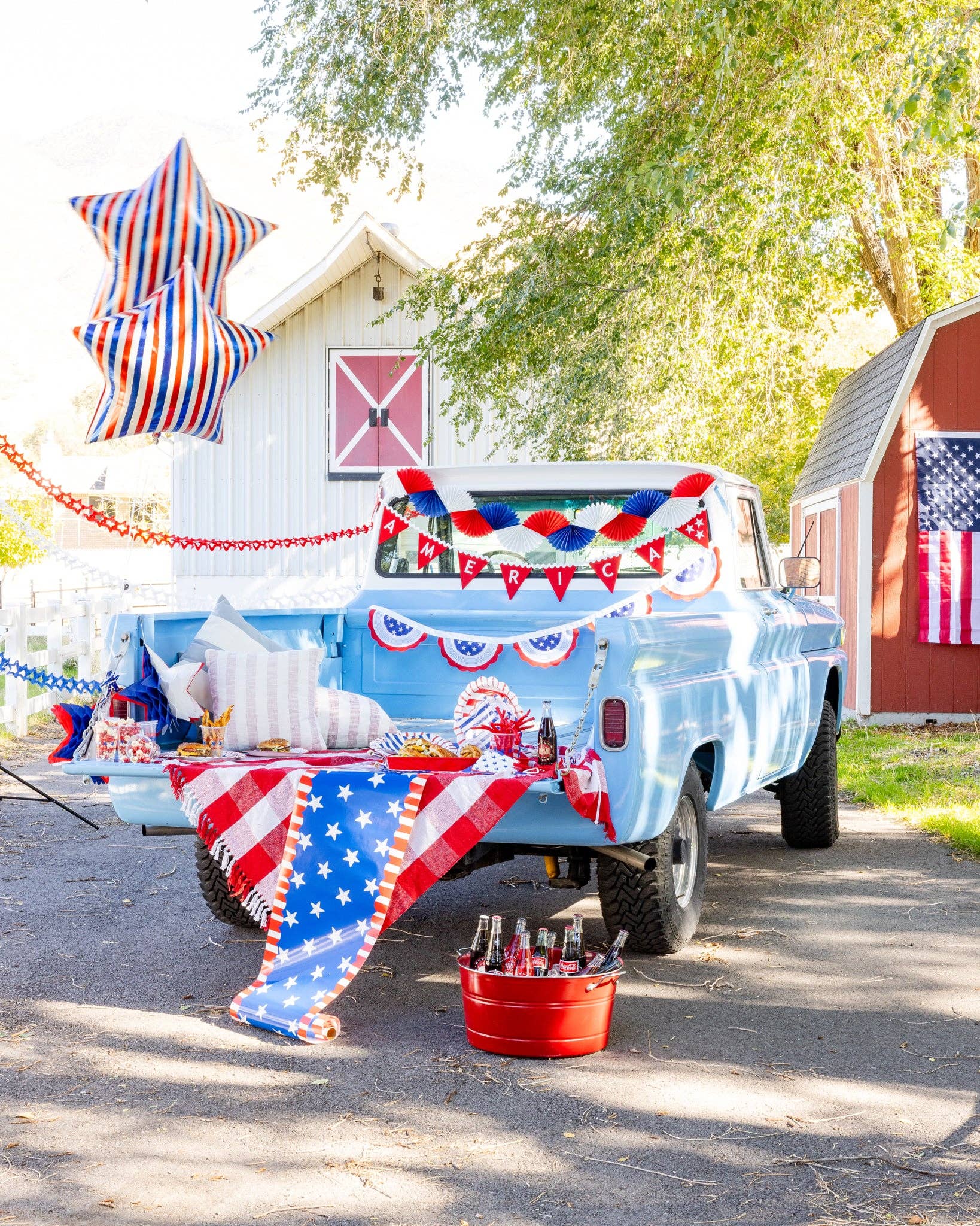 Red white and blue striped star mylar balloon floating above a styled 4th of July truck bed picnic with patriotic banners plates and party decor
