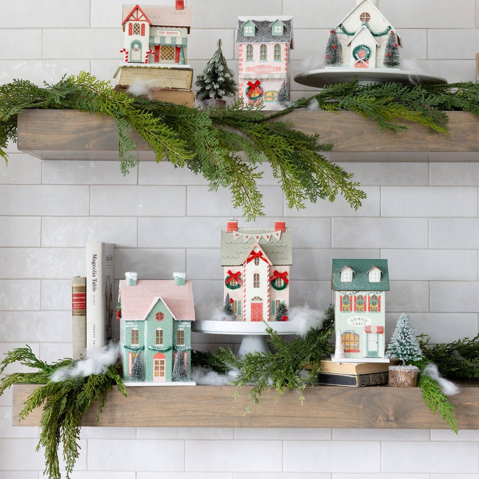 Retro Christmas decor village collection styled on two white kitchen shelves with garland, showing multiple houses and a church.