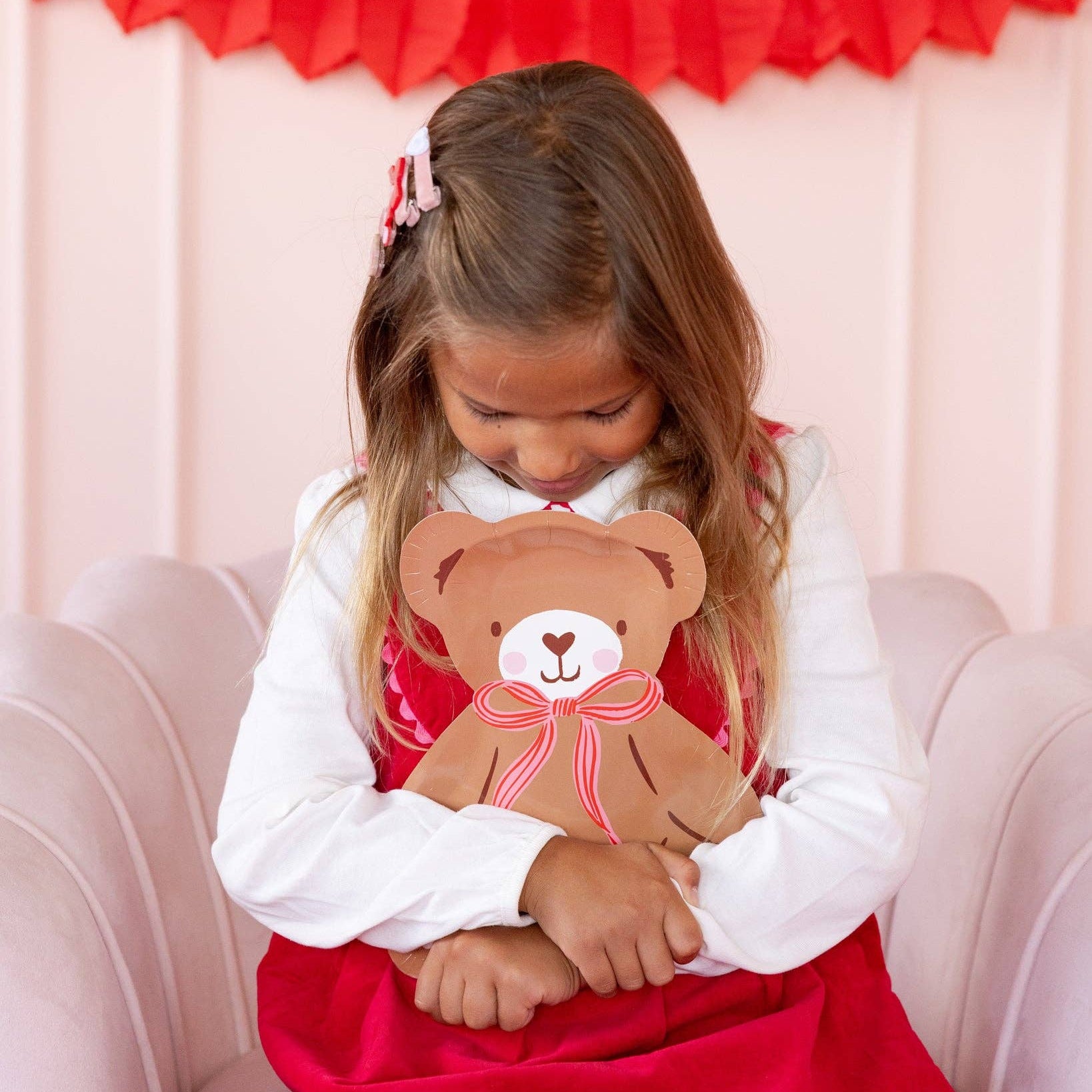 Child holding teddy bear-shaped plate while sitting in chair