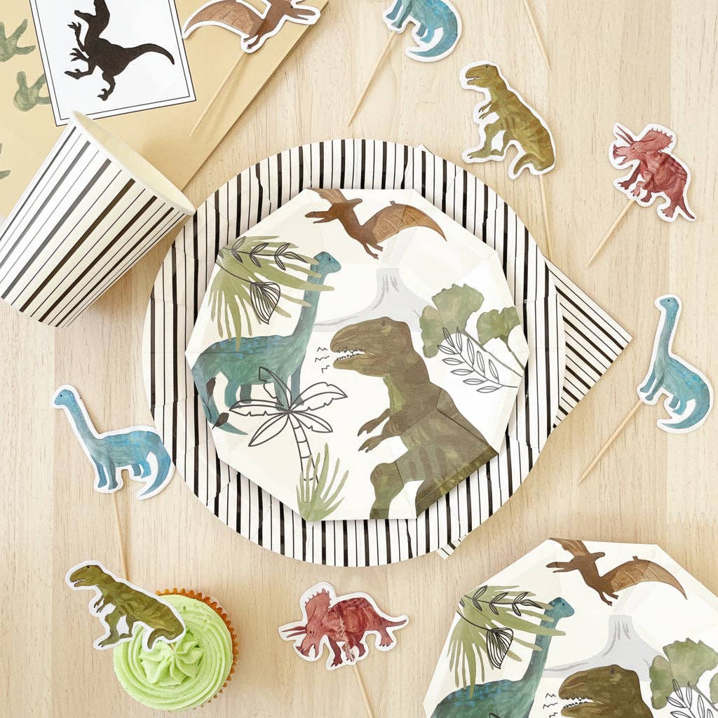 Overhead flat lay of dinosaur party plates and cups with assorted dino toppers