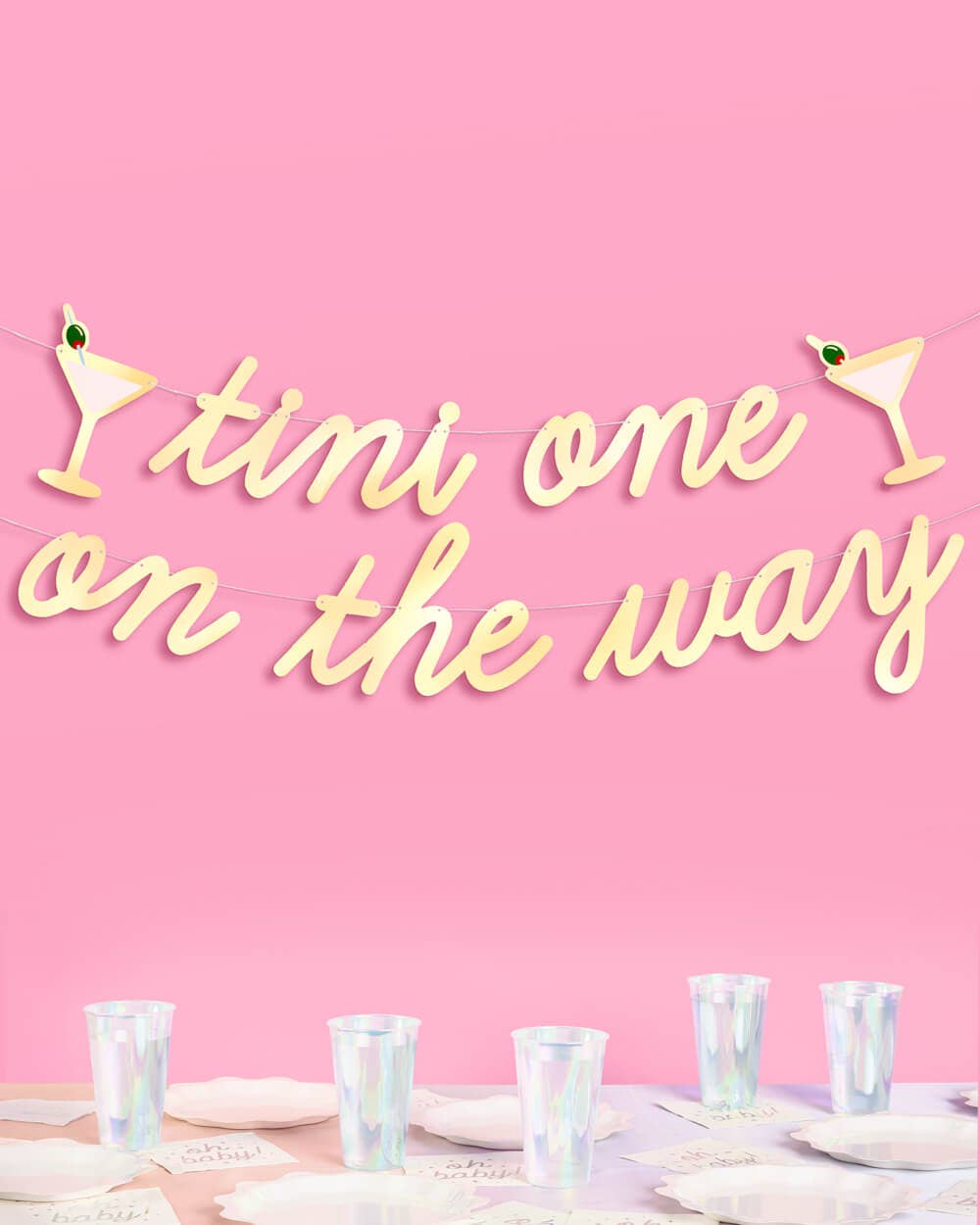 Tini One on the Way gold foil banner hung above baby shower table with cups and napkins