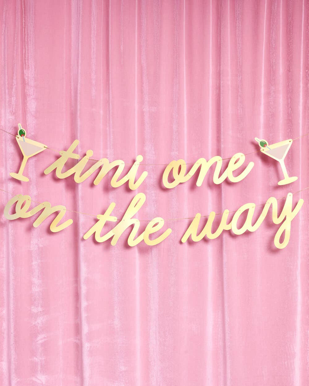 Full Tini One on the Way gold foil banner with martini glass accents hung on pink velvet backdrop