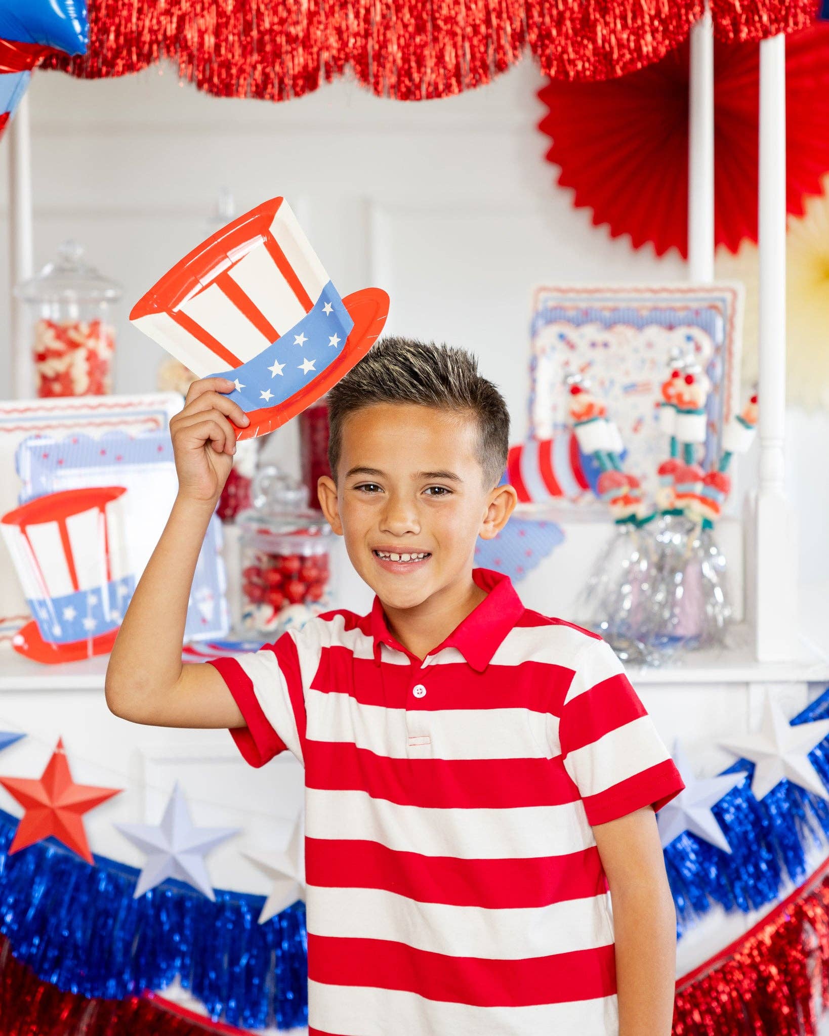 Child smiling and holding Uncle Sam hat shaped paper plate above his head at a red white and blue party