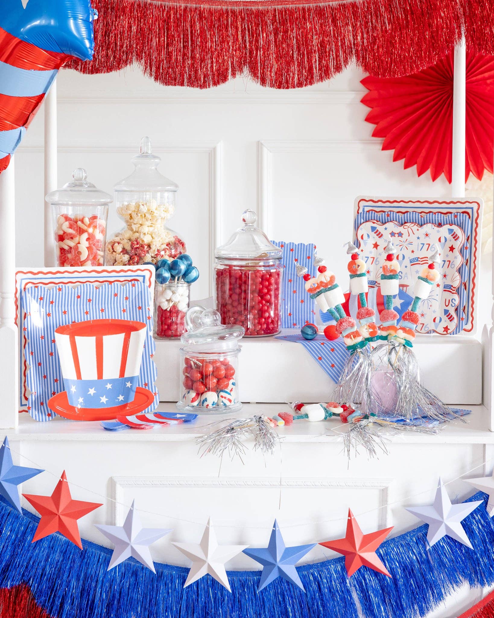 Close-up of Fourth of July party cart tabletop showing Uncle Sam hat shaped paper plates alongside coordinating Americana plates, candy jars, and candy kabobs