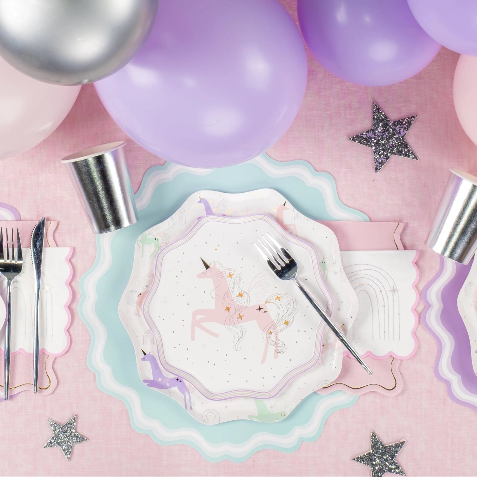 Place setting with pink unicorn plate, rainbow napkin, and balloons—perfect unicorn birthday party look.