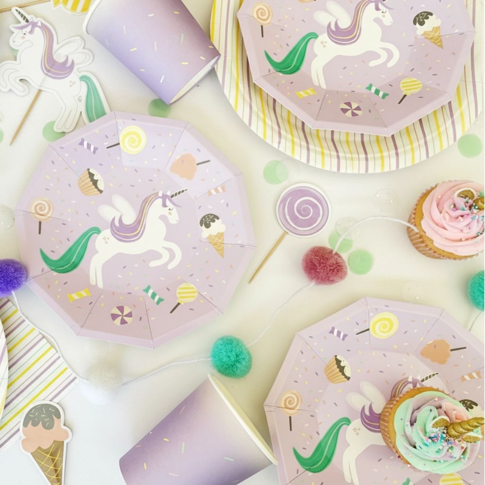 Overhead view of unicorn plates and cups with pastel party confetti